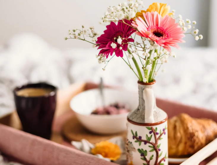 Breakfast tray with flower vase, coffee, croissant and bowl of granola