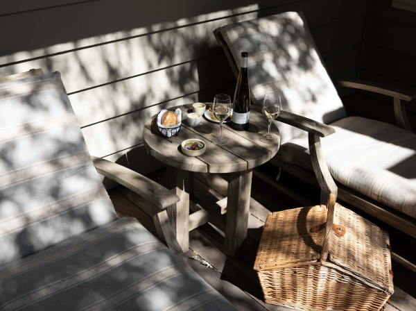 Outdoor picnic set up with chaise lounge chairs and table with food and glasses of wine