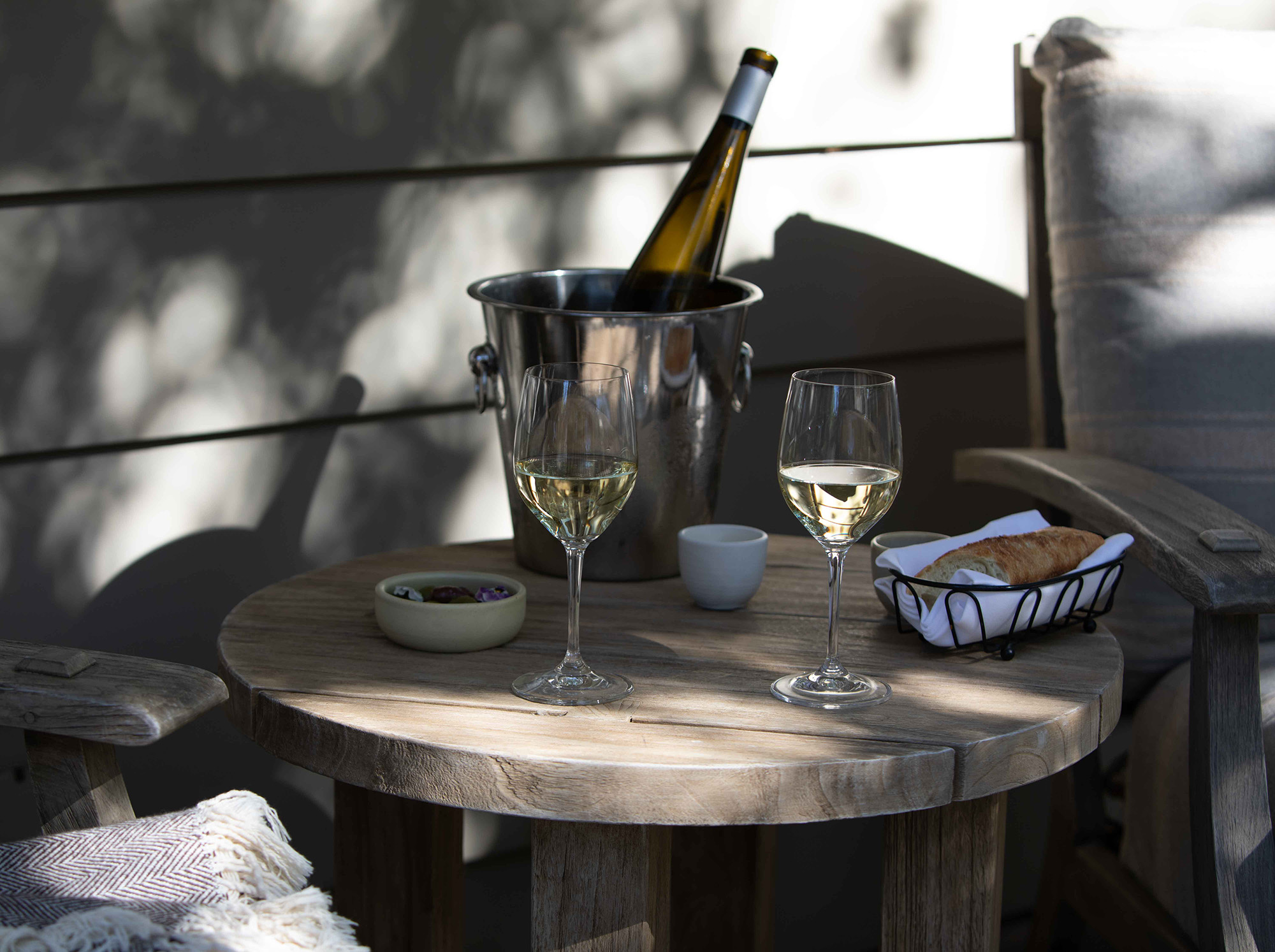 Small outdoor table with wine glasses and bread and two lounge chairs