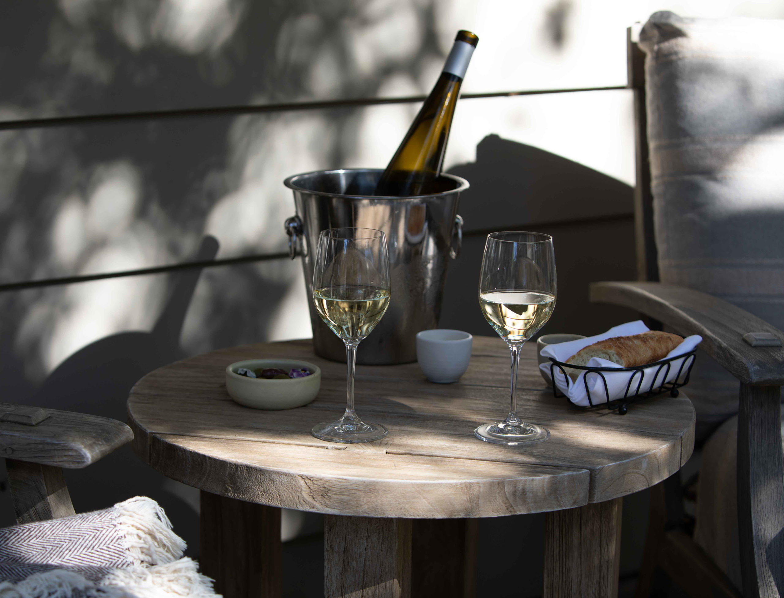 Small outdoor table with wine glasses and bread and two lounge chairs