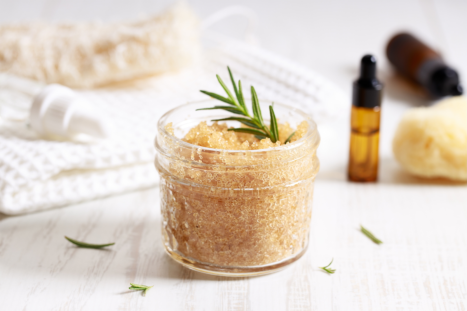 Spa setting showing container of a scrub along with towels and essential oils in the background.
